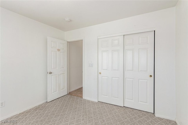 unfurnished bedroom with baseboards, light carpet, and a closet
