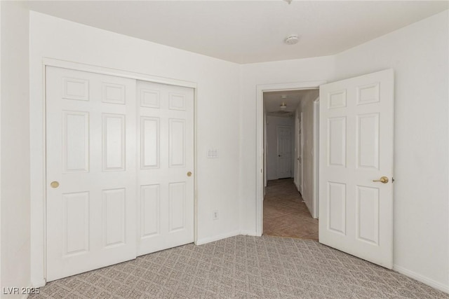 unfurnished bedroom featuring baseboards, light carpet, and a closet
