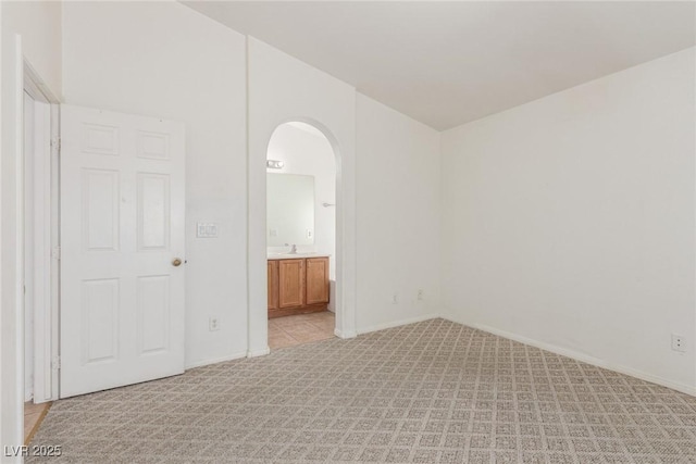 unfurnished room featuring baseboards, arched walkways, and light carpet