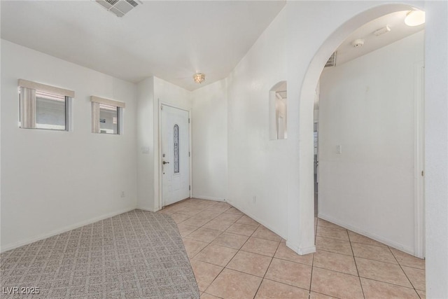 foyer featuring baseboards, arched walkways, visible vents, and light tile patterned floors
