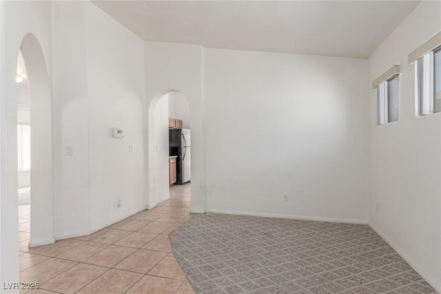 unfurnished room featuring baseboards, arched walkways, a high ceiling, and light tile patterned floors
