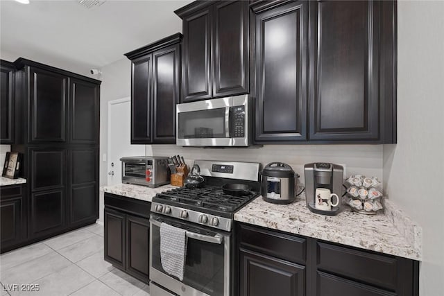 6247 Milford Sound St, Las Vegas, NV 89148 - kitchen with stainless steel appliances, dark cabinetry, light tile patterned floors, and light stone countertops