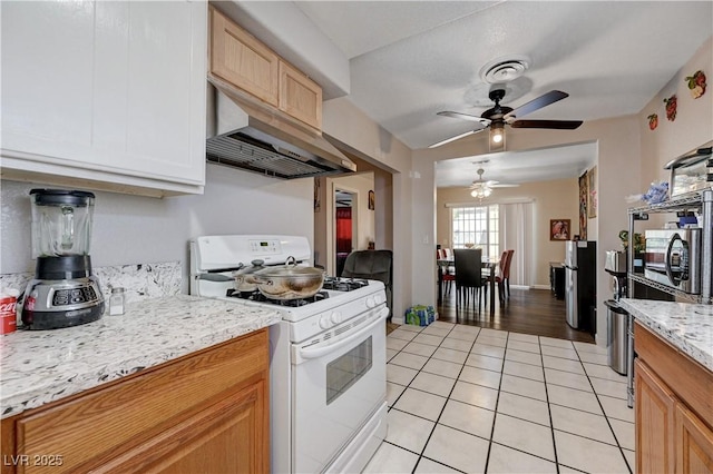 kitchen with under cabinet range hood, light tile patterned floors, white range with gas stovetop, ceiling fan, and light stone counters