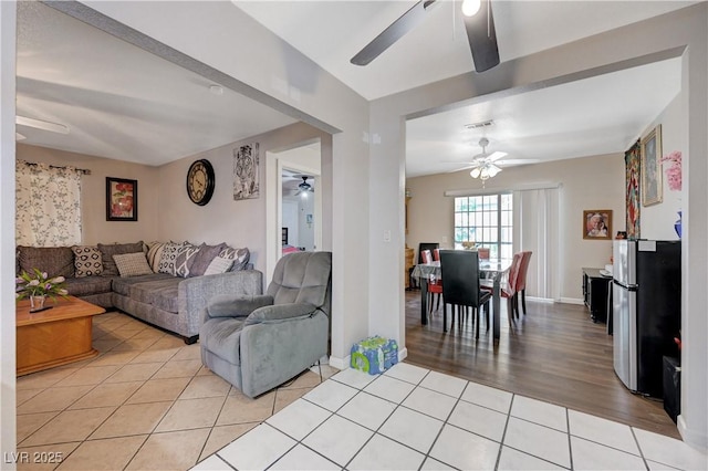 living area featuring light tile patterned floors, a ceiling fan, and baseboards