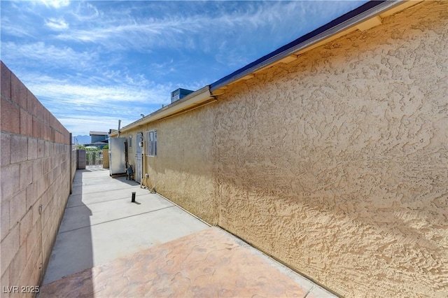 view of side of property with stucco siding, fence, and a patio area