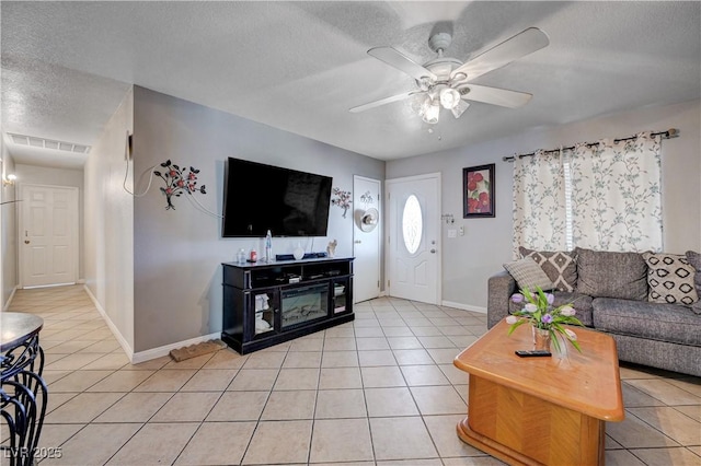 living area featuring light tile patterned floors, a textured ceiling, visible vents, ceiling fan, and baseboards