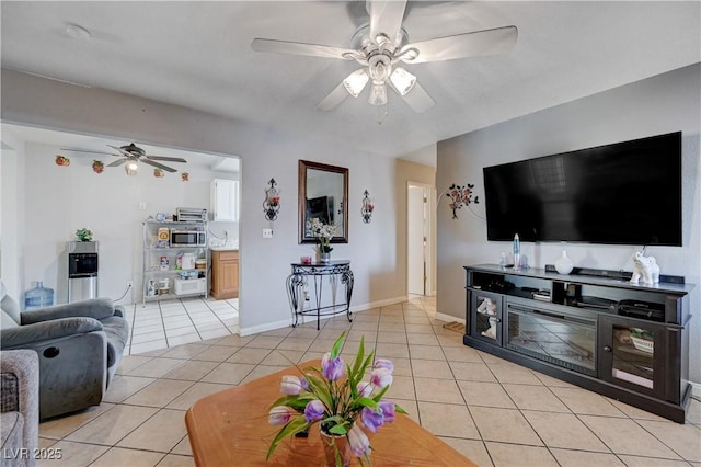 living area with baseboards, light tile patterned floors, and ceiling fan