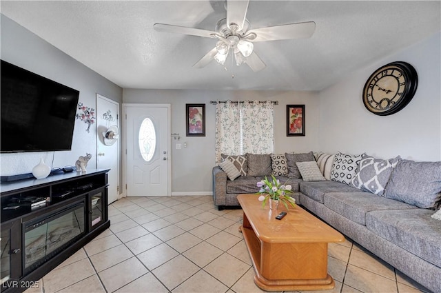 living room with light tile patterned flooring, a ceiling fan, a textured ceiling, and baseboards