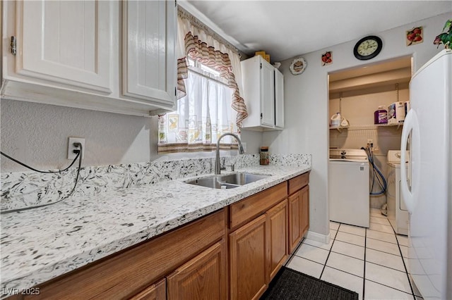 kitchen featuring freestanding refrigerator, independent washer and dryer, brown cabinetry, a sink, and light tile patterned flooring