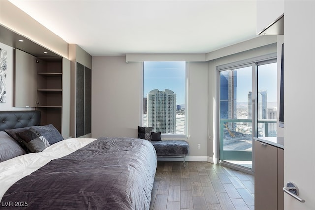 bedroom with wood finished floors, a city view, access to outside, and baseboards