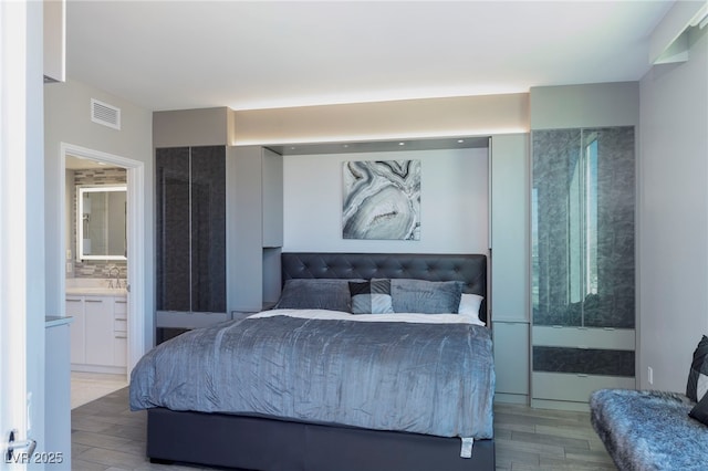 bedroom with visible vents, wood finished floors, connected bathroom, and a sink