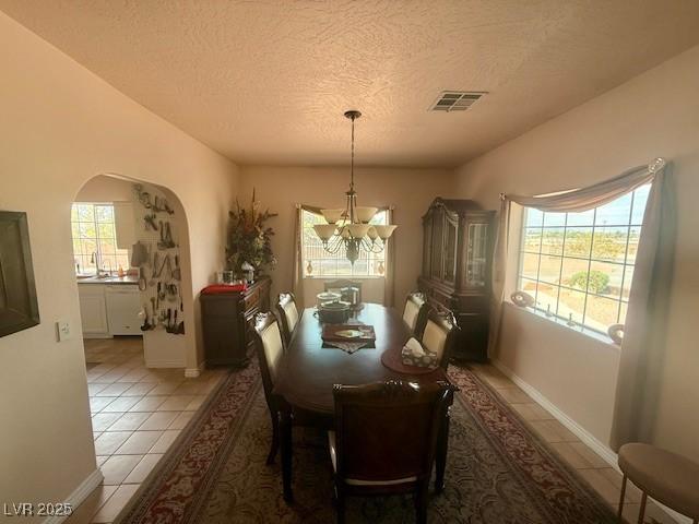 10561 Rancho Destino Rd, Las Vegas, NV 89183 - dining area with light tile patterned flooring, arched walkways, a textured ceiling, a chandelier, and visible vents