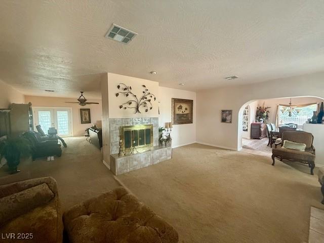 10561 Rancho Destino Rd, Las Vegas, NV 89183 - living room with a textured ceiling, visible vents, arched walkways, a tile fireplace, and carpet flooring