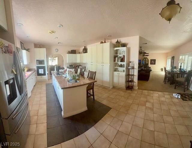 10561 Rancho Destino Rd, Las Vegas, NV 89183 - kitchen with black oven, white cabinetry, built in microwave, stainless steel fridge with ice dispenser, and light tile patterned floors