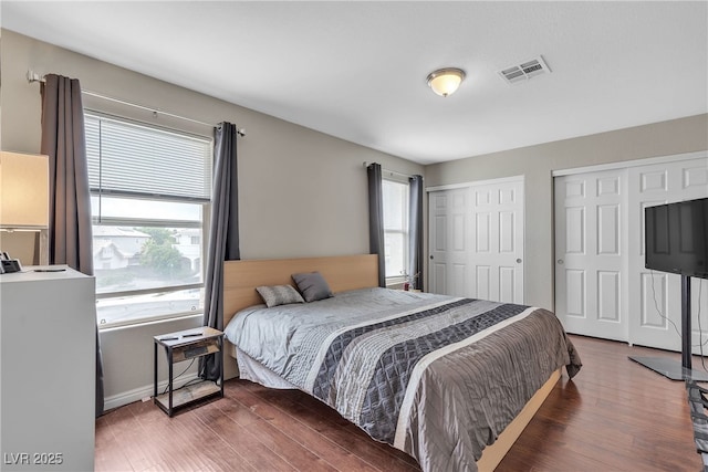 bedroom with wood finished floors, visible vents, baseboards, and multiple closets