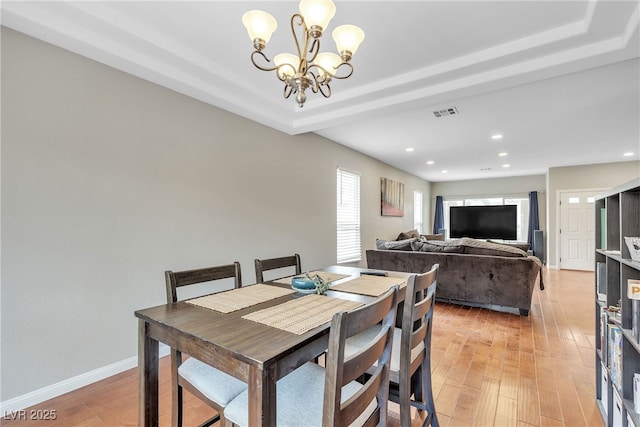 dining room featuring light wood-style flooring, a tray ceiling, visible vents, baseboards, and a notable chandelier
