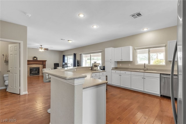 kitchen with stainless steel appliances, visible vents, a ceiling fan, a sink, and a glass covered fireplace