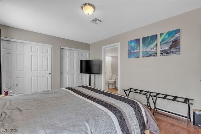 bedroom featuring ensuite bath, wood finished floors, visible vents, and two closets