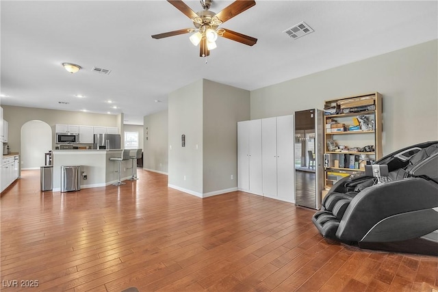 living room featuring ceiling fan, arched walkways, visible vents, and light wood-type flooring