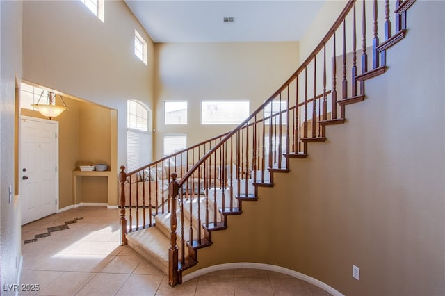 stairs with tile patterned flooring, baseboards, a towering ceiling, and visible vents