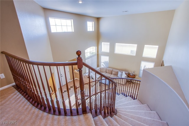 stairway featuring baseboards, carpet, and a high ceiling