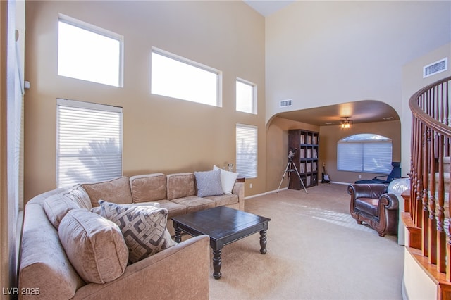 living area with visible vents, arched walkways, a towering ceiling, and light carpet