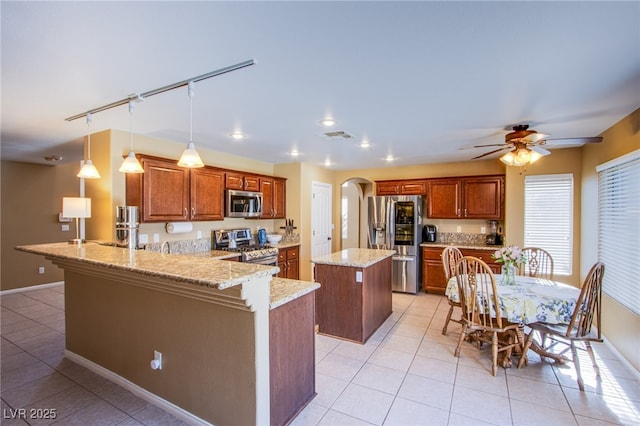 kitchen featuring light tile patterned flooring, appliances with stainless steel finishes, arched walkways, a peninsula, and a kitchen island