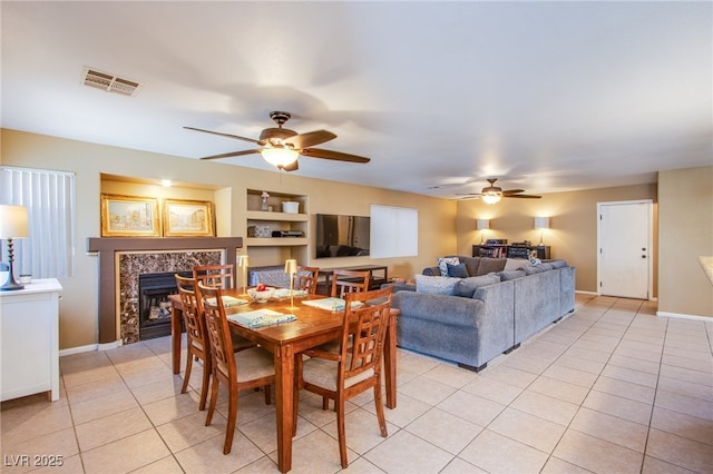 dining room featuring visible vents, baseboards, ceiling fan, a tiled fireplace, and light tile patterned floors