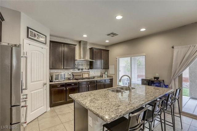 kitchen with wall chimney range hood, a kitchen bar, light tile patterned floors, a sink, and stainless steel appliances