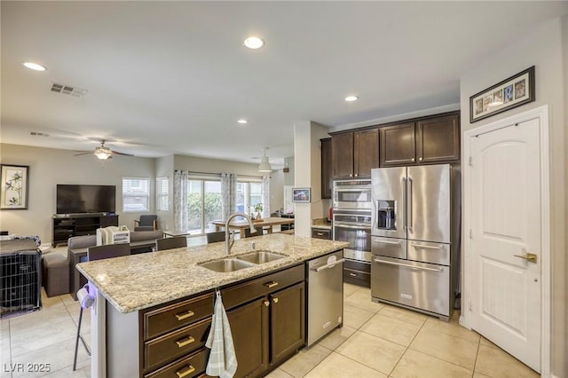 kitchen with dark brown cabinetry, light stone countertops, a center island with sink, a sink, and stainless steel appliances