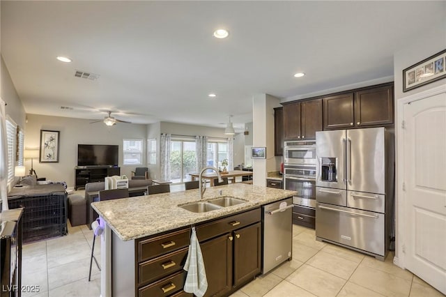 kitchen with visible vents, a kitchen island with sink, dark brown cabinets, a sink, and appliances with stainless steel finishes