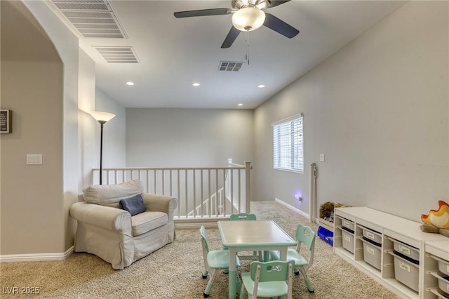 living area with visible vents, carpet flooring, ceiling fan, and an upstairs landing
