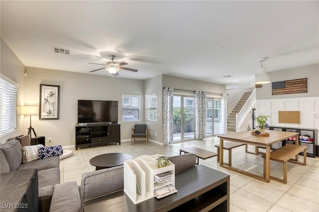 living area featuring a ceiling fan, visible vents, light tile patterned floors, baseboards, and stairs