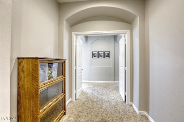 corridor featuring carpet floors, baseboards, and arched walkways