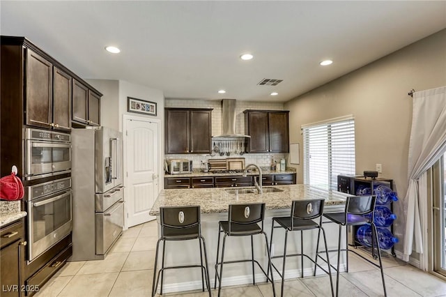 kitchen featuring appliances with stainless steel finishes, a breakfast bar, a sink, wall chimney exhaust hood, and tasteful backsplash