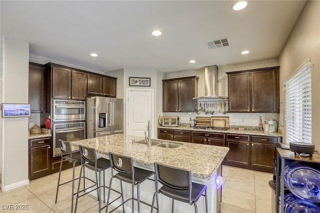 kitchen with wall chimney range hood, a sink, stainless steel appliances, backsplash, and visible vents