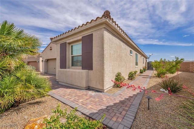 view of side of property with stucco siding, an attached garage, and fence