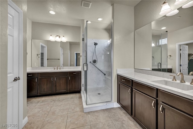 full bath featuring a sink, two vanities, visible vents, tile patterned flooring, and a shower stall