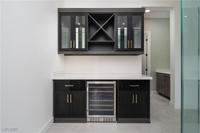 bar with light tile patterned flooring, beverage cooler, a bar, and baseboards