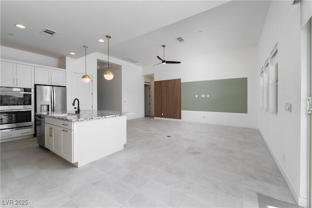 kitchen featuring stainless steel appliances, a sink, a ceiling fan, light stone counters, and decorative light fixtures