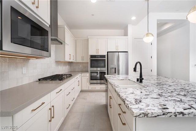 kitchen with tasteful backsplash, a sink, white cabinets, wall chimney exhaust hood, and appliances with stainless steel finishes