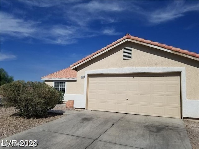 ranch-style house with a garage, a tile roof, stucco siding, and driveway