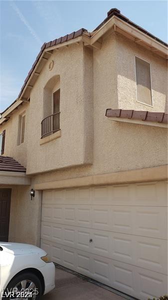 view of side of property featuring an attached garage, a tile roof, a balcony, and stucco siding