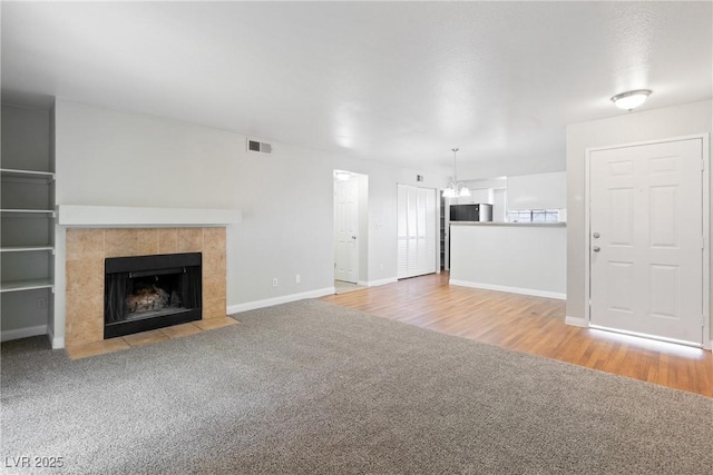 unfurnished living room with a chandelier, carpet, visible vents, baseboards, and a fireplace