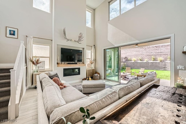 living room featuring a glass covered fireplace, a high ceiling, stairs, and wood finished floors