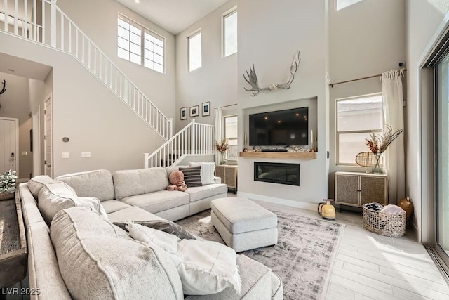 living area with stairs, a towering ceiling, wood finished floors, and a glass covered fireplace