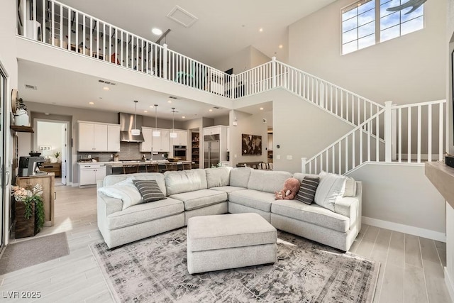 living room featuring light wood-style floors, recessed lighting, stairs, and a towering ceiling