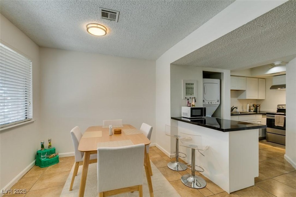 5725 Smoke Ranch Rd Unit A, Las Vegas, NV 89108 - kitchen with white cabinets, a peninsula, a textured ceiling, electric range, and stacked washing maching and dryer