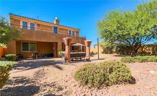 rear view of property with a chimney, a patio, a balcony, and stucco siding