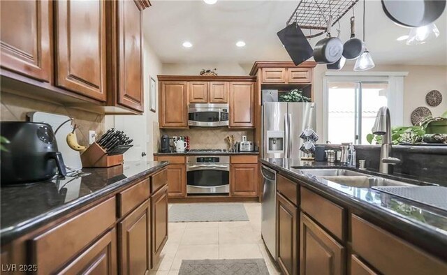 kitchen with dark stone counters, a sink, decorative backsplash, brown cabinets, and appliances with stainless steel finishes